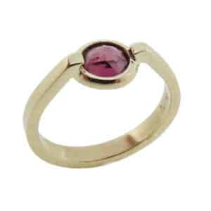 A custom designed ring in 14 karat yellow gold showcasing an inverted bezel set 1.10 carat round brilliant cut rhodolite garnet. Created by our jeweler and owner, David Blitt as part of our Studio Tzela line. This is uniquely perfect to represent January birthdays.