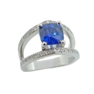 18K white gold custom lady's split shank ring by Studio Tzela claw set with a 2.02ct cushion shape blue sapphire and accented along the bands with 40 pave set round brilliant cut diamonds, 0.262cttw.