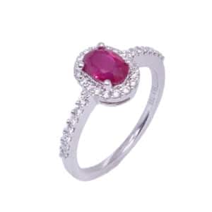 A halo ring in 18 karat white gold, showcasing a 0.99 carat oval shaped Ruby. Accented with diamonds totaling 0.24 carats. This ring is a perfect gift to represent July birthdays and 40th anniversaries.