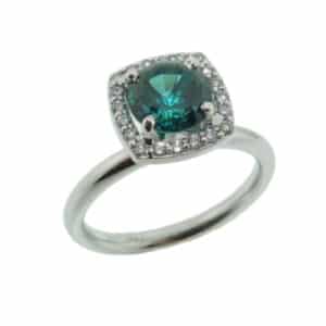 A 14 karat white gold halo ring, showcasing a 1.46 carat teal green tourmaline. Surrounded by diamonds totaling 0.05 carats. The perfect gift for 8th anniversaries.