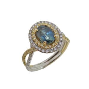 18K white and yellow gold split shank engagement ring, set with an oval brilliant 1.34ct blue-green sapphire. Accented with 46 round brilliant cut natural yellow diamonds, 0.32 carat total weight, SI1 -SI2 and with 50 round brilliant cut diamonds, 0.40 carat total weight, VS2-SI1, G/H.