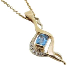 14K white and yellow gold custom pendant by Studio Tzela semi-bezel set with a 0.549ct oval shape aquamarine and accented with 5 round brilliant cut diamonds, 0.038cttw.