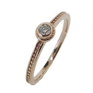 14K rose gold stackable ring with milgrain detail. Bezel set with a 0.084 carat round brilliant cut Hearts On Fire diamond
