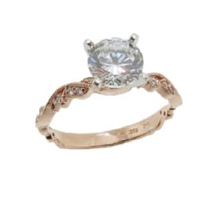 14 karat rose and white gold vintage solitaire design engagement ring accented by 22 = 0.12ctw round brilliant cut diamonds. This unique design has stunning milgrain engraving and scroll work design and is a great alternative to a traditional solitaire ring. Priced without a center gemstone. Let us find you the perfect center that fits your tastes and budget!