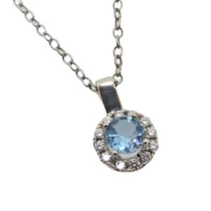 14 karat white gold pendant set with an aquamarine and accented by a halo of 0.155ctw of round brilliant cut diamonds.
