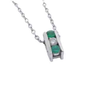14K white gold pendant set with a 0.10ct I/J, SI2, excellent cut round brilliant cut diamond and 2 emeralds, 0.202cttw.