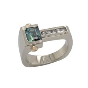 14K white and yellow gold custom lady's ring by Studio Tzela with bezel set with a 1.148ct emerald cut blue/green sapphire and 5 = 0.15cttw princess cut diamonds.  Sapphire is the birthstone for September.