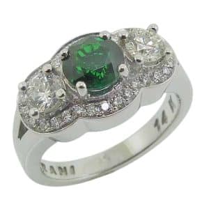 14 Karat white gold three stone ring featuring a 1.14 carat Tsavorite and accented with two ideal cut round brilliant cut diamonds, 0.483cttw, I, SI1 and accented on the side and in the halo with 30 very good cut round brilliant cut diamonds, 0.25cttw, G/H, SI1.