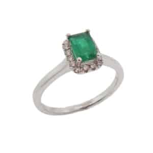 Lady's halo ring in 14K White gold set with one 0.63 emerald in emerald cut and accented with sixteen G-H, SI1-2 round brilliant cut diamonds totaling 0.13 carats.