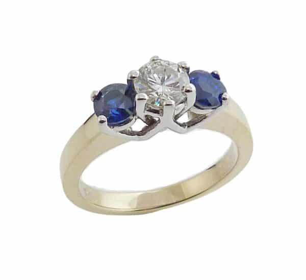 14K White and yellow gold engagement ring claw set with a 0.51 carat I, I1 very good cut, round brilliant cut diamond and accented on each side with two round blue sapphires, totalling 0.98 carat.