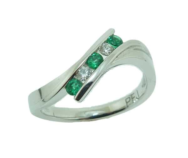 Lady's 18K white gold bypass style ring set with three round emeralds totaling 0.16 carats and two round brilliant cut diamonds totaling 0.09 carats.