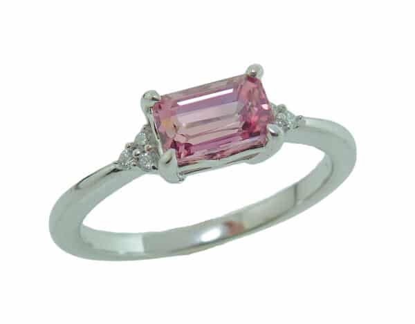 14 karat white gold ring featuring a 1.28ct oval emerald cut Padparadscha sapphire and accented with 6 = 0.05cttw of round brilliant cut diamonds.