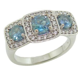 Lady's 14K white gold ring set with one 0.62 carat blue/green round sapphire and two totaling 0.67 carats, accented on the halo with thirty-eight pave set round brilliant cut diamonds totaling 0.27 carats, F-G, VS.