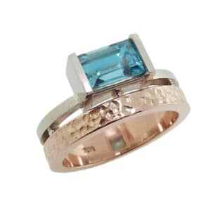 14K white and rose gold lady's double band ring featuring a bar-set 2.115 carat emerald cut blue zircon with hammered and polish texture.