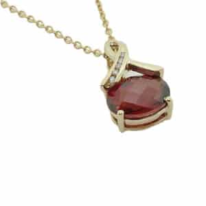 14K yellow gold pendant claw set with a 1.5ct oval checkerboard cut garnet and five channel set round brilliant cut diamonds, 0.03 total carat weight.
