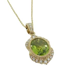 14K Yellow gold antique style halo pendant with milgrain details placed on a 16" chain. Bezel set in the middle is an oval peridot, 1.97 carat, and twenty-two claw and pave round brilliant cut diamonds, 0.18cttw, in the halo and on the bale.