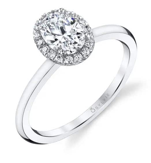 14 Karat white gold engagement ring "Elsie" by Sylvie Collection. Set with a 0.75 carat oval CZ and with round brilliant cut diamonds on the halo totaling 0.12 carats, G/H, VS-SI. Available in 14K gold, 18K gold, or platinum. This ring can be made in any combination of white, pink or yellow gold and can be customized to accommodate different size and shape diamonds, by special order. Priced without a center gemstone. Let us find you the perfect center that fits your tastes and budget!