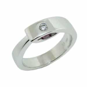 14K white gold lady's ring flush set with one 0.058 carat, G-H, SI1 round brilliant cut diamond and accented in the profile with two round rubies totaling 0.231 carats.