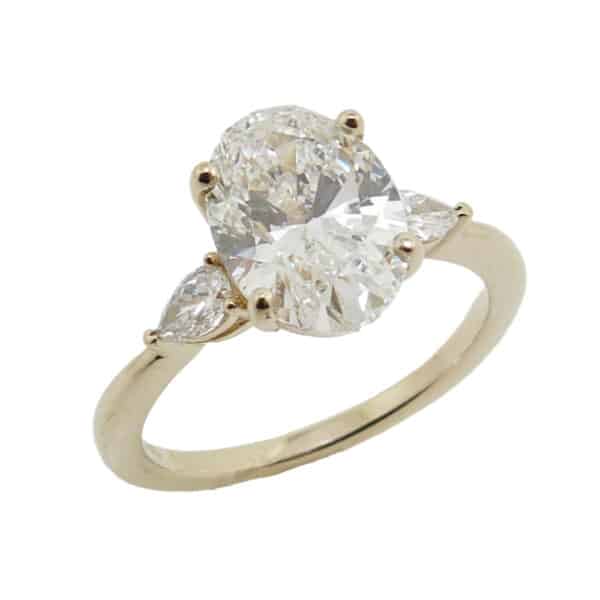 14K Yellow gold three stone engagement ring set in the centre with a 2.06 carat, E, VS1 oval brilliant cut lab grown diamond and accented on the sides with two pear shape lab grown diamonds, 0.19 total carat weight.