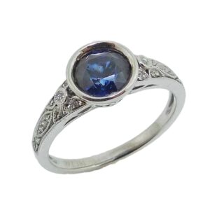 14K White gold ring bezel set with one 1.46 carat round deep blue sapphire and accented on the band with round brilliant cut diamonds, totalling 0.05 carats, SI, H.