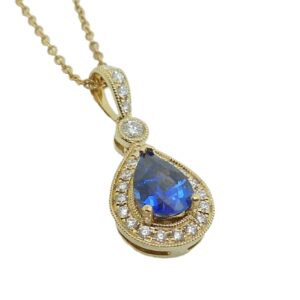 14K Yellow gold pendant set with 0.87 carat pear shape blue sapphire and accented in the halo with twenty-three round brilliant cut diamonds totaling 0.20 carats, G-H, SI1.