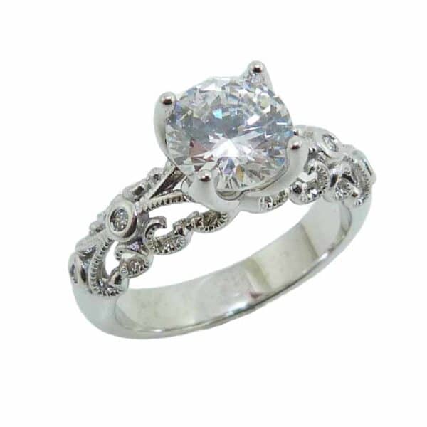 14K White gold filigree engagement ring set in the centre with a 1.5 carat CZ and accented on the sides with four round brilliant cut lab grown diamonds, 0.04 total carat weight. Priced without a center gemstone. Let us find you the perfect center that fits your tastes and budget! Available in 14K gold, 18K gold, or platinum. This ring can be made in any combination of white, pink or yellow gold and can be customized to accommodate different size and shape diamonds, by special order.