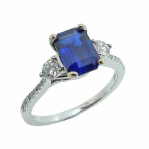 18K White gold ring claw set in the centre with a 1.45 carat emerald cut blue sapphire and accented with twenty excellent-very good cut, round brilliant cut diamonds totaling 0.38 carats, G-H VS-SI.