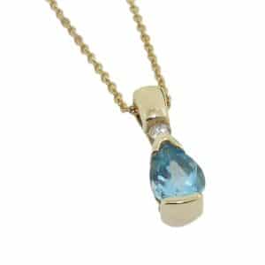 14 Karat yellow gold pendant set with one 7x5mm pear shaped blue topaz and one 0.04 carat round brilliant cut diamond, G/H, SI.