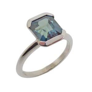 14K White gold lady's ring semi-bezel set with a 3.23 carat emerald cut green/blue sapphire.