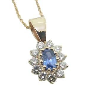 14K Yellow gold halo pendant claw set in the centre with a 0.656 carat oval blue sapphire and accented in the halo with eleven round brilliant cut natural diamonds, totaling 0.676 carats, H, SI1-2.