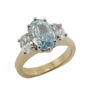 14K Yellow and white gold custom three stone engagement ring claw set in the center with one fancy vivid blue oval modified brilliant lab grown diamond, 2.06 carat, VS1. Accented on the side with two claw set oval brilliant cut lab grown diamonds, totaling 0.65 carats, F/G, VS1-2.