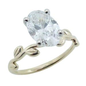 14K Yellow and white gold solitaire engagement ring with leaf details on the band, claw set in the centre with a 2.13 carat, E, VVS2 oval brilliant cut lab grown diamond.