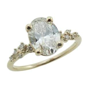 14K Yellow gold scattered diamond engagement ring claw set with a 1.50 carat oval lab grown diamond D, VVS2 and accented with ten lab grown round brilliant cut diamonds on the band, 0.10cttw, E/F, VS+.