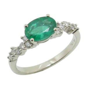 14K White gold scattered diamond band lady's ring claw set in an east-west orientation with a 0.96 carat oval emerald and accented on the band with twelve natural round brilliant cut diamonds, 0.23cttw, G/H, SI1-2.