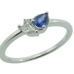 14K White gold asymmetrical lady's ring set with one blue pear shape sapphire, 0.20ct; one marquise brilliant cut diamond, 0.08ct; and a round brilliant cut diamond, 0.02ct.