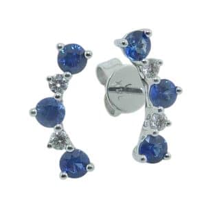 14K White gold curved line studs claw set with six sapphire's, 0.57 total carat weight, and four round brilliant cut diamonds, 0.09 total carat weight.