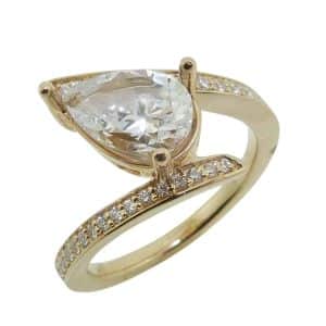 14K Yellow gold bypass style engagement ring set in the centre with a 1.5 carat pear shape CZ and accented on band with 0.24cttw pave set round brilliant cut diamonds.
